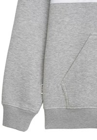 Detailní záběr na rukáv a kapsu šedé mikiny s žebrovanými manžetami a malou bílou textilní etiketou na bočním švu.