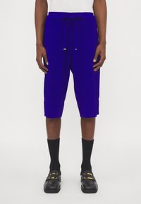 Blauwe katoenen shorts met een elastische tailleband en trekkoorddetail. Gekenmerkt met zwarte kniekousen en zwarte instappers met gouden accenten.