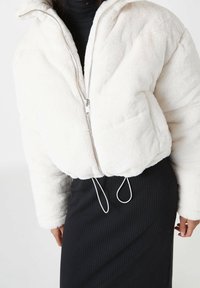 Chaqueta tipo puffer de piel sintética blanca con cierre de cremallera en el frente, con un dobladillo ajustable y un corte relajado, combinada con una falda negra de canalé.