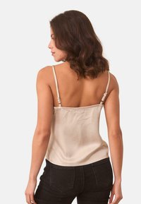Camiseta de satén beige con tirantes ajustables, textura suave y diseño ajustado, combinada con jeans de tiro alto negros.