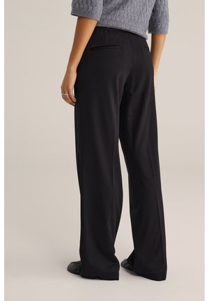 Fekete, bő szárú nadrág sima textúrával, két visszafogott hátsó zsebbel, szürke kötött felsővel párosítva.