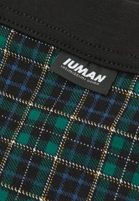 Svart rutig tyg med ett rutmönster i grönt, blått och gult. Inkluderar en tagg med "Intimissimi Uomo"-logotypen högst upp.