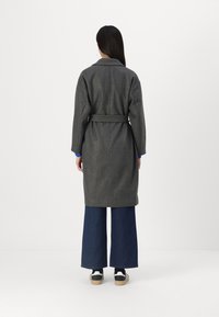 Grijze wollen jas met een tailleband, een getailleerde pasvorm, lange mouwen en een reverskraag, gecombineerd met donkerblauwe wijde jeans en sneakers.