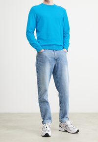 Himmelblå crewneck-tröja i bomullsblandning, med långa ärmar. Bärs med ljusblå denimjeans och vita sneakers. Avslappnad passform.