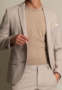 Beżowa marynarka z teksturowanym wykończeniem, w połączeniu z jasnobeżowym t-shirtem. Zawiera poszetkę. Slim fit, dopasowany fason.