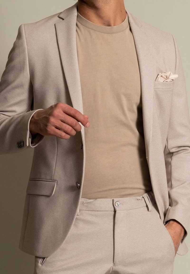 Beżowa marynarka z teksturowanym wykończeniem, w połączeniu z jasnobeżowym t-shirtem. Zawiera poszetkę. Slim fit, dopasowany fason.