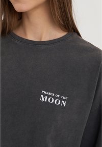 Dark gray long-sleeve t-shirt with a round neckline and a faded texture. The front features white text that reads "PHASES OF THE MOON."