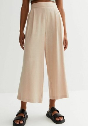 Beige wide-leg cropped pants worn with black double-strap sandals and a cropped top, shown on a standing person against a plain background.