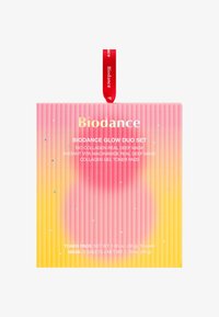 Zestaw Biodance Glow Duo w opakowaniu z gradientowym wzorem w odcieniach różu i żółci, z złotym napisem, czerwoną wstążką i dekoracyjnymi akcentami w kształcie gwiazdek.
