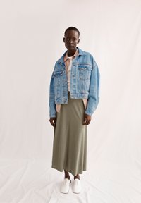 Denim jacket in light blue with a cropped design, layered over a striped shirt, paired with a long olive green skirt and white shoes.