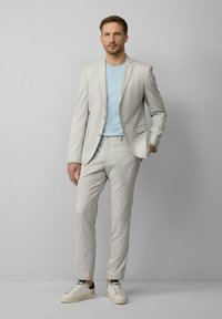 Hellgraues kariertes Anzug mit slim-fit Design, kombiniert mit einem blauen Hemd und weißen Sneakern. Glatte Textur und maßgeschneiderte Passform.