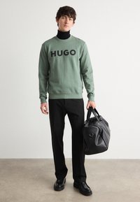 Grønn genser med "HUGO" logo, svart turtleneck, svarte bukser og svart veske. Glatt stoff, avslappet passform og minimalistisk design.