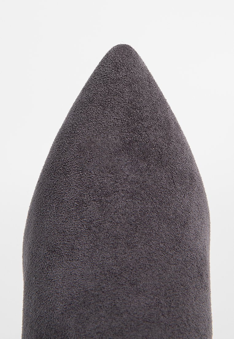 Scarpa a punta in suede grigio scuro, con una texture liscia e una silhouette elegante. Nessun hardware o motivo visibile.