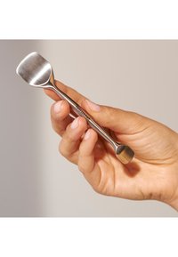 Mano che tiene un piccolo spatola in acciaio inossidabile a doppia estremità con punte piatte e quadrate su entrambi i lati.