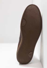 Suela de zapato de cuero marrón con un patrón texturizado y estriado. Presenta un detalle de logotipo circular y un borde de color marrón claro. Diseño limpio y plano.