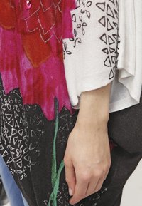 Suéter de punto con un vibrante patrón floral en rosa y rojo, con acentos geométricos en negro. Corte holgado y textura suave.