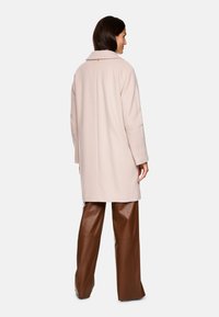 Helle rosa Wolljacke mit strukturiertem Design, weitem Kragen und langen Ärmeln, kombiniert mit braunen Leder-Hosen mit weitem Bein. Minimalistischer Stil.