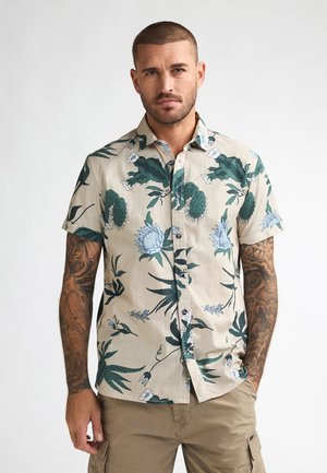 Koszula z krótkim rękawem w kolorze beżowym z kwiatowym wzorem, przedstawiającym zielone i niebieskie motywy roślinne, zapinana na guziki z przodu, wykonana z fakturowanej tkaniny.