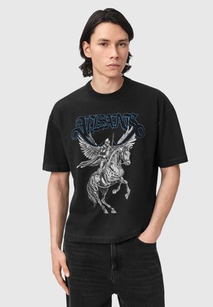 Jonge man met zwart haar die een zwart T-shirt draagt met een gedetailleerde afbeelding van een gevleugelde bepantserde ridder op een steigend paard en de tekst "ALLSAINTS" erboven.
