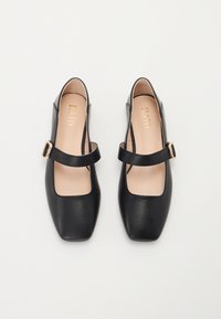 Chaussures Mary Jane en cuir noir avec un bout carré, dotées d'une lanière étroite et d'un accent en boucle dorée. Texture lisse et design minimaliste.