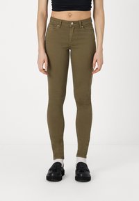 Jeans slim fit en verde oliva, fabricados con algodón elástico, que cuentan con bolsillos frontales, un cierre de botón y detalles de costura sutiles.
