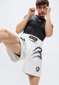 Λευκά αθλητικά σορτς με μαύρο γραφικό λιονταριού και διαγώνιες ρίγες, σετ με εφαρμοστή μαύρη κοντομάνικη μπλούζα. Ορατή ελαστική μέση.