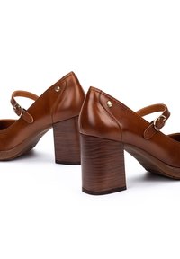 Chaussures à talons en cuir marron avec une lanière et une boucle. Présentent un bout fermé, une forme arrondie et des talons en bois texturé.