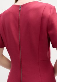 Vue de dos d'une personne portant une robe rouge ajustée à manches courtes avec une fermeture éclair argentée visible au centre.