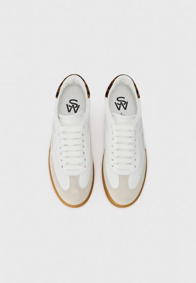Vita sneakers med en mockatåspets och ovandel i läder, med en sula av gummin och kontrasterande mönstrade detaljer på hälen.