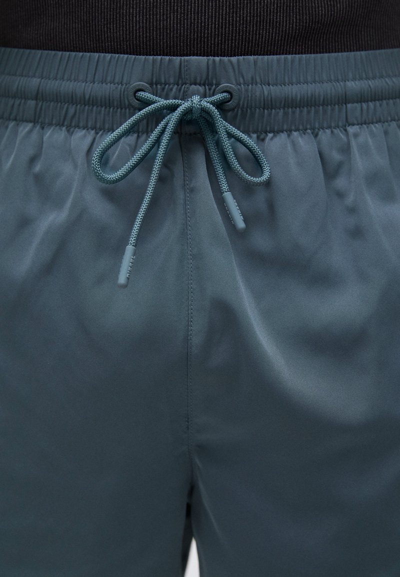 Mesh zwemshorts in donker teal, met een elastische tailleband en een trekkoordsluiting. Gladde textuur met een subtiele glans.