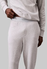 Lichtgrijze joggers met een zachte textuur, voorzien van een brede elastische tailleband waarop "Calvin Klein" staat. Comfortabele pasvorm met zijzakken.