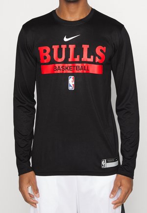 Osoba nosząca czarną koszulkę z długim rękawem z czerwonym "Bulls Basketball," białym logo Nike i logo NBA z przodu.