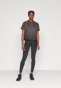 Μαύρο αθλητικό μπλουζάκι με υφασμάτινο σχέδιο, συνδυασμένο με εφαρμοστά μαύρα κολάν. Και τα δύο ρούχα έχουν κομψή, μοντέρνα εμφάνιση με ελάχιστες λεπτομέρειες.