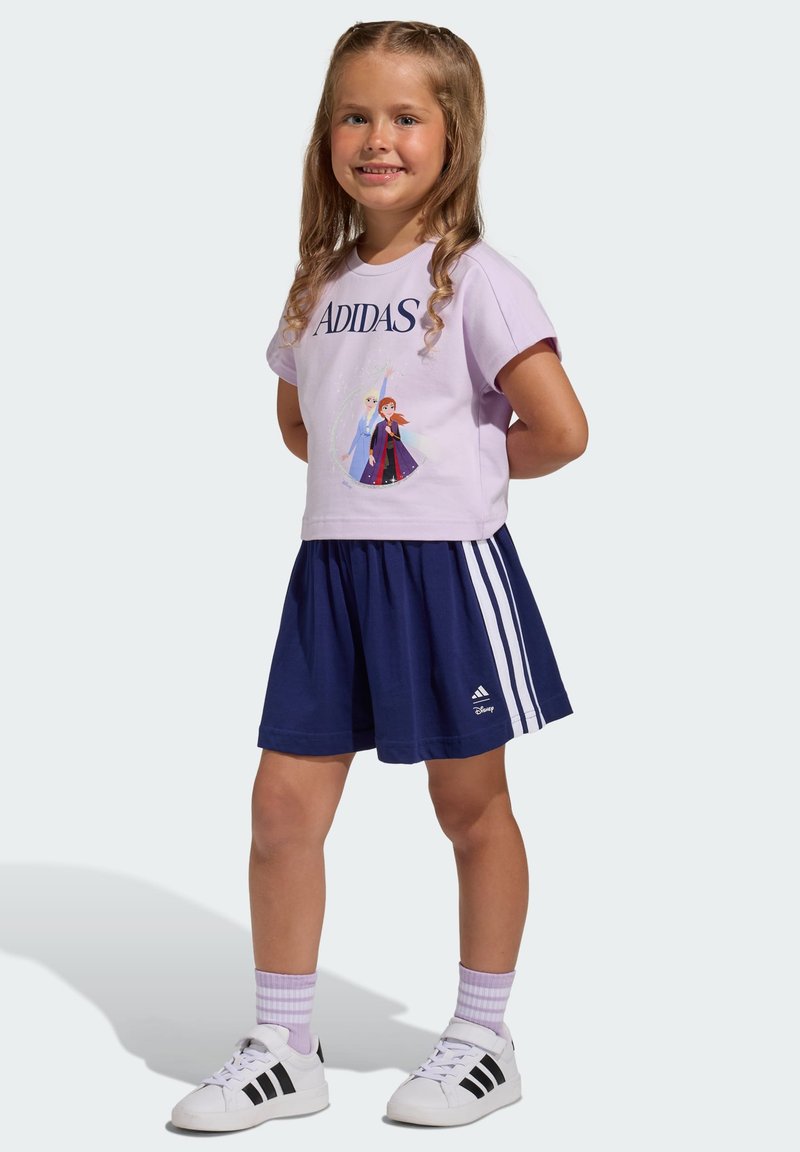 Svetlofialové tričko s logom "ADIDAS" a postavičkami Disney; tmavomodrá sukňa s tromi bielymi pruhmi; biele tenisky s čiernymi detailmi.