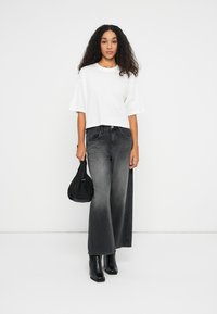 Hvid, struktureret cropped top parret med højtaljede, vide, falmede sorte jeans; sorte ankelstøvler; holder en lille sort taske.