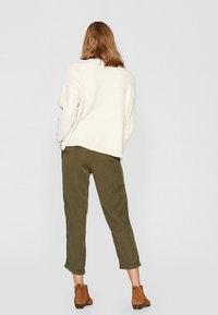 Crème, getextureerde oversized sweater gecombineerd met olijfgroene cropped broek en bruine enkellaarsjes, gezien vanaf de achterkant.