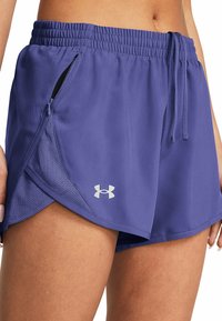 Kvinna i lila sportshorts med sidofickor och Under Armour-logotyp på vänster höft, som visar mitten av låret och midjan.