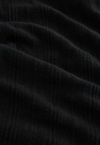 Tissu noir côtelé avec des plis doux et un motif texturé courant verticalement sur la surface.