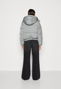 Polstret grå jakke med hætte, der har et cropped design og elastisk talje, parret med højtaljede sorte brede jeans.