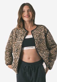 Bomberjakke med leopardmønster, blød tekstur, sort kant og knaplukning. Bæres over en sort sports-bh og grå sweatpants.