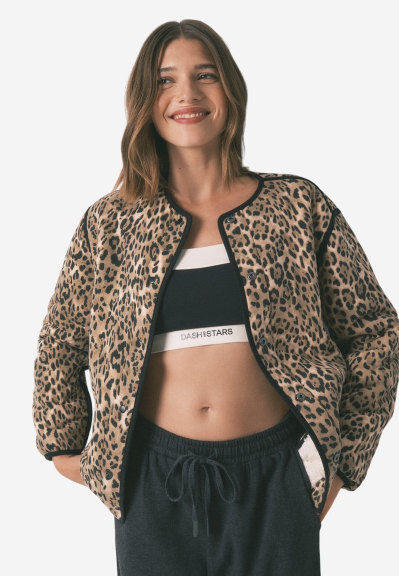 Bomberjakke med leopardmønster, blød tekstur, sort kant og knaplukning. Bæres over en sort sports-bh og grå sweatpants.