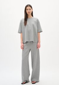Grijze gekorte oversized t-shirt en wijde broek van zachte stof. Minimalistisch ontwerp met korte mouwen en een comfortabele pasvorm. Zwarte sandalen.