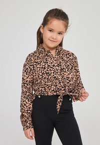 Camicia leggera con stampa leopardata in tonalità di rosa e nero, dotata di una chiusura frontale con bottoni e vita annodata. Abbinata a pantaloni neri attillati.