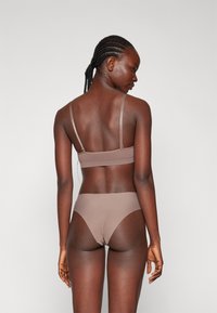 Grudnjak i bikini komplet u svijetlosmeđoj boji. Mekani materijal, minimalistički dizajn s tankim trakama i glatkom teksturom, s niskim rezom.