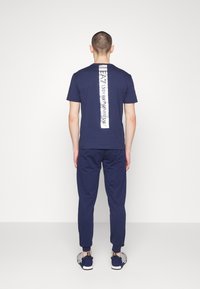 Navyblå bomullströja med en vertikal reflekterande logopanel på baksidan, i kombination med matchande joggingsbyxor och sportskor.