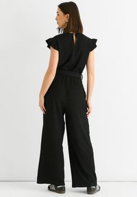 Black textured jumpsuit with short ruffle sleeves, elastic waistband, and wide legs. Features a keyhole opening at the back.