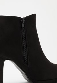 Stivaletto nero con tacco alto in materiale scamosciato, dotato di zip laterale, texture liscia e silhouette elegante.