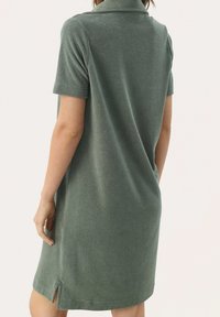 Robe polo verte douce à manches courtes, avec un col, offrant une coupe décontractée et des fentes latérales pour un confort de mouvement. Tissu texturé.