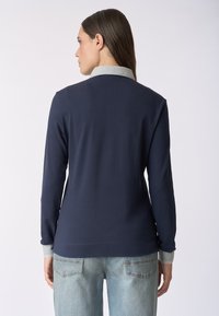 Maglietta a maniche lunghe blu navy con colletto e polsini grigio chiaro, caratterizzata da un design semplice e una texture morbida. Abbinata a jeans azzurri.