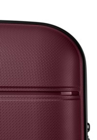 Close-up of the textured surface and rounded corner of a burgundy hard-shell suitcase with black trim.